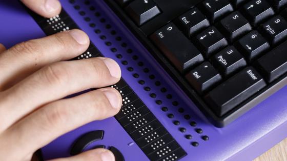 Blind person using computer with braille computer display and a computer keyboard. Blindness aid, visual impairment, independent life concept.